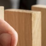 Man stopping domino effect on wooden table